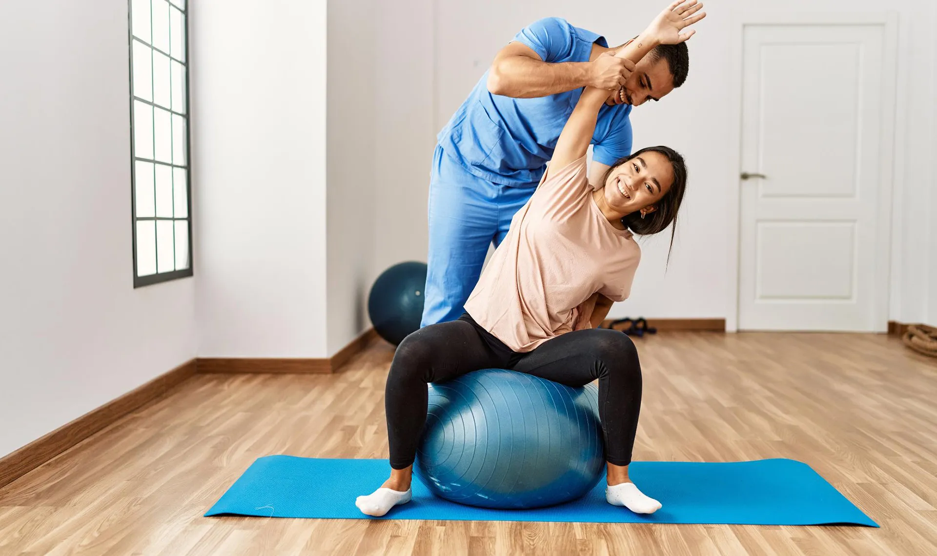 Bewegungstherapie im Reha-Zentrum Bad Aussee – Physiotherapeut unterstützt Patientin bei Dehnübung auf Gymnastikball